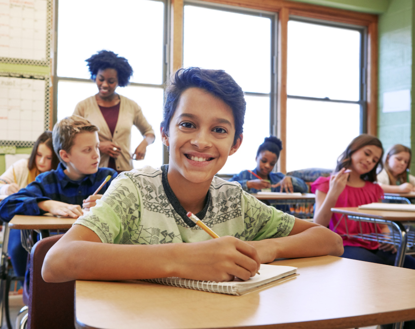 A young boy is working at a desk in a classroom.