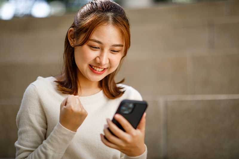 A young woman is looking at her phone and clenching her fist in excitement. 
