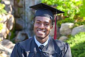 A young man is posing in his college graduation cap and gown. 