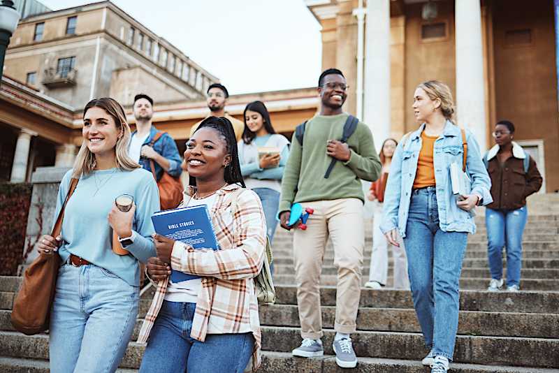 A group of college students are walking down the steps outside of a building. 