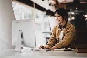 A young woman is participating in online learing at her desktop computer.