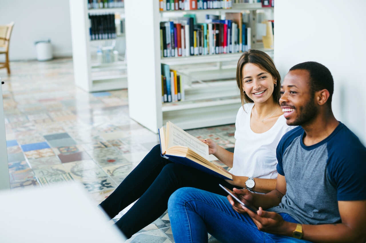 Two students sitting on the floor in a library