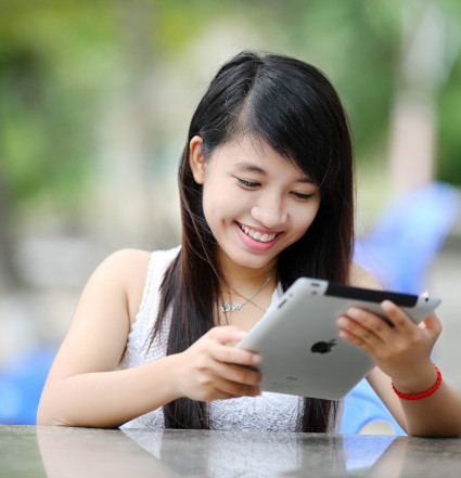 A young woman is looking at a tablet smiling. 