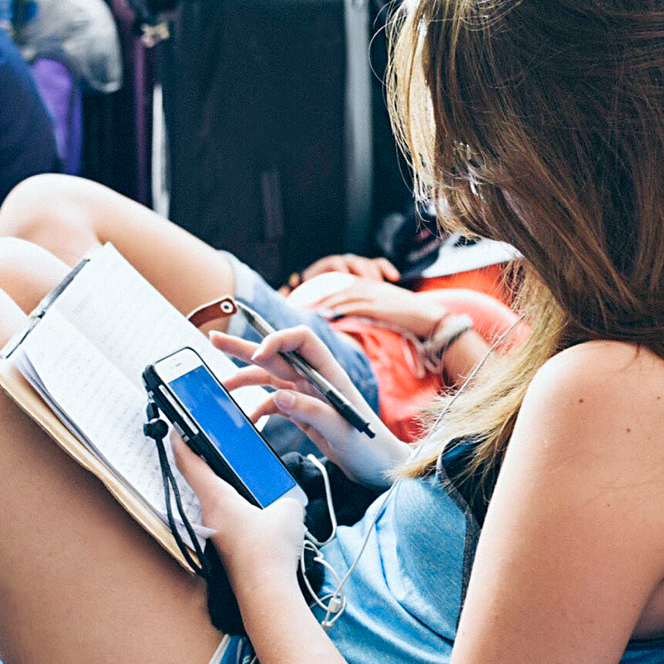 A person is on their phone and working in a notebook. 
