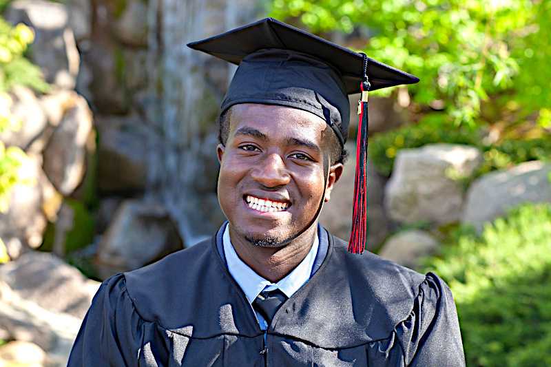 A young man is posing in his college graduation cap and gown. 